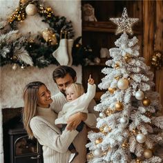 a man and woman holding a baby near a christmas tree