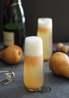 a tall glass filled with liquid next to some pears