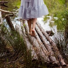 a woman walking across a fallen log in the woods