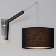 a wall light with a black shade hanging from it's side on the wall