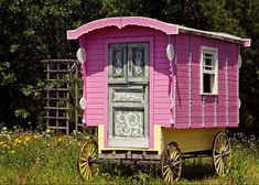 a pink and yellow cart sitting on top of a grass covered field next to trees