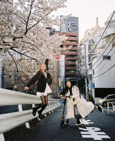 two women walking down the street with cherry blossom trees in the background