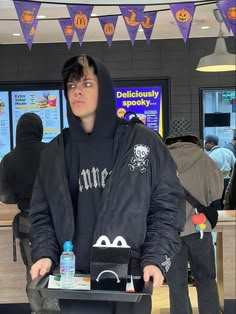 a young man in a black hoodie holding a tray with food on it and looking at the camera