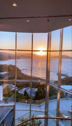 the sun is setting over the ocean from inside a building with large windows that look out onto the water