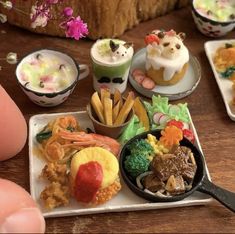 miniature food items displayed on trays with fingers pointing at them and finger tips in the foreground