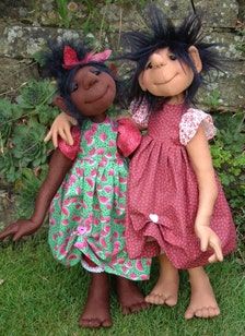 two dolls standing next to each other in the grass