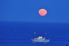 a boat in the ocean with a full moon rising over it's back side