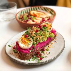 a white plate topped with food next to a bowl filled with fruit and veggies