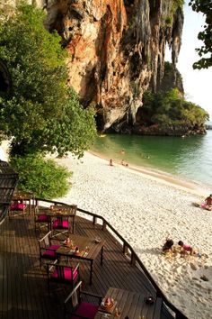 people are sitting at tables on the beach next to the water and cliffs in the background