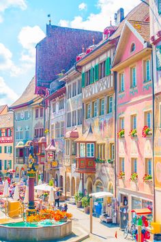 an old european town with colorful buildings and flowers on the fountain in front of it