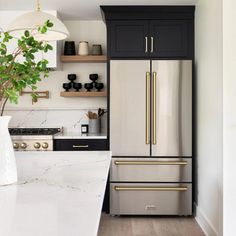 a kitchen with black cabinets and white marble counter tops, gold trim on the refrigerator