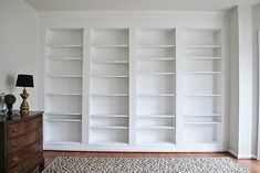 an empty room with white bookcases on the wall and a rug on the floor