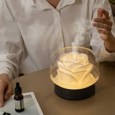 a woman is sitting at a table with a rose lamp