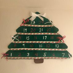 a wooden christmas tree with numbers and bows on the top, hanging from a wall