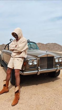 a man sitting on top of a car in the desert with his head covered by a hoodie