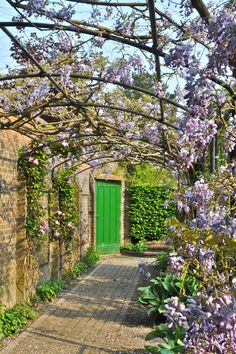 a green door surrounded by purple flowers and greenery on the side of a brick building