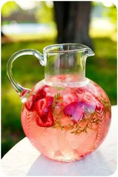 a pitcher filled with water and strawberries on top of a white tablecloth covered table