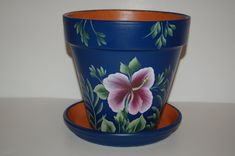 a blue flower pot sitting on top of a white table next to a cup with an orange rim