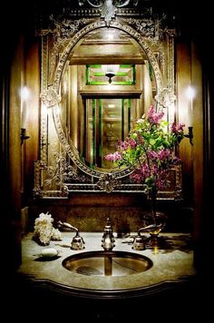 a bathroom sink sitting under a mirror next to a vase with flowers on top of it