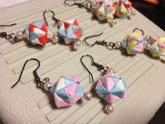 four origami earrings with pearls and beads on top of an object that is sitting on a table