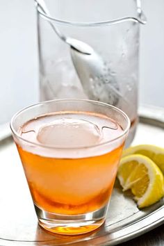 a glass filled with liquid sitting on top of a metal tray next to a lemon wedge