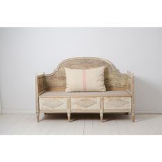 an old wooden bench with two pillows on top of it and a white wall in the background