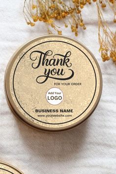 thank you for your order logo in a round tin on a white tablecloth next to some dried flowers