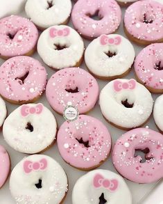 there are many pink and white donuts with bows on them in a box together