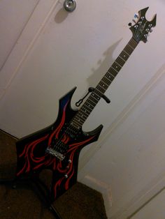 a black and red guitar sitting on top of a stand next to a white wall