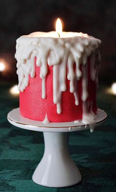 a red cake with white icing and a lit candle