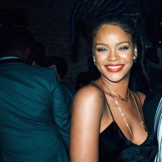 a woman in a black dress standing next to a man with dreadlocks on