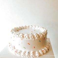 a white frosted cake with sprinkles sitting on top of a table