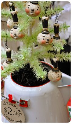 a small christmas tree in a white ceramic pot with ornaments hanging from it's sides