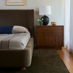 a bed sitting next to a night stand on top of a wooden dresser in a bedroom