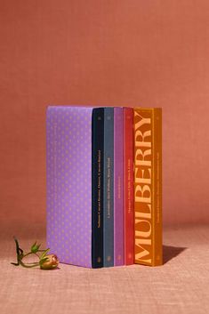 three books sitting next to each other on top of a pink tableclothed surface