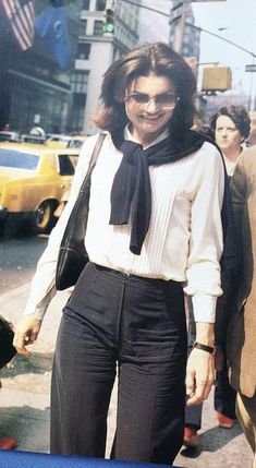 a woman in white shirt and black pants walking down street with other people behind her