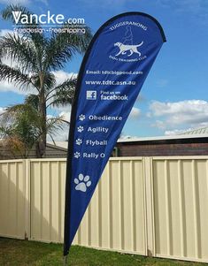 a blue flag with white writing on it in front of a fence and palm tree