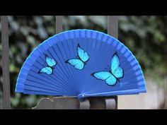 a blue fan with butterflies painted on it sitting in front of a metal fence post