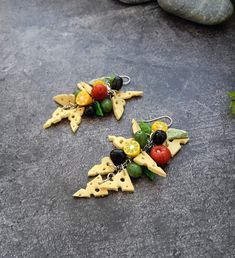 two pieces of fruit and cheese dangling from earwires on concrete surface next to rocks