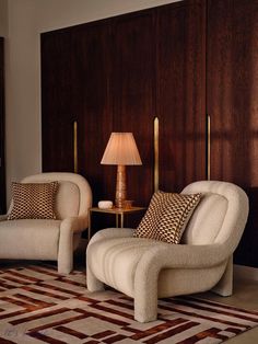 two chairs and a lamp in a room with wood paneling on the wall behind them