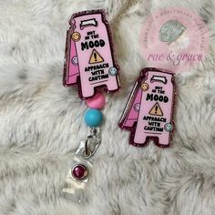 two pink luggage tags are attached to a white furry surface with a blue bead charm