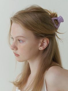 a woman with long hair wearing a white top and purple bow in her hair is looking off to the side