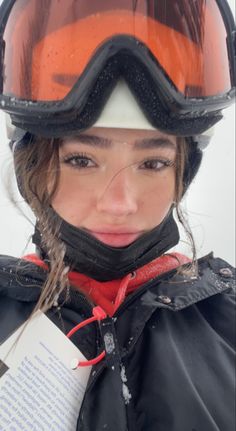 a young woman wearing ski goggles and a snowboarder's helmet is looking at the camera