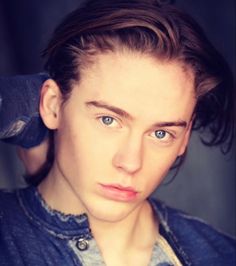 a man with long hair and blue eyes is looking at the camera while wearing a denim jacket