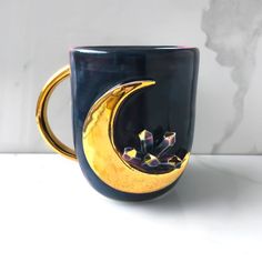 a coffee cup with a crescent moon on the side and flowers in the middle, sitting on a white surface