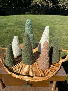 four knitted trees in a wicker basket on a wooden table with grass behind them