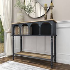 a console table with books on it in front of a large mirror and white rug