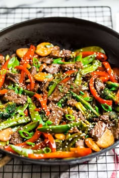 a skillet filled with beef and vegetables on a cooling rack next to a wooden spoon