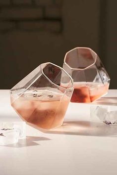 two clear vases filled with liquid sitting on top of a white table next to ice cubes