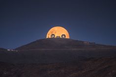 the full moon is seen over a hill